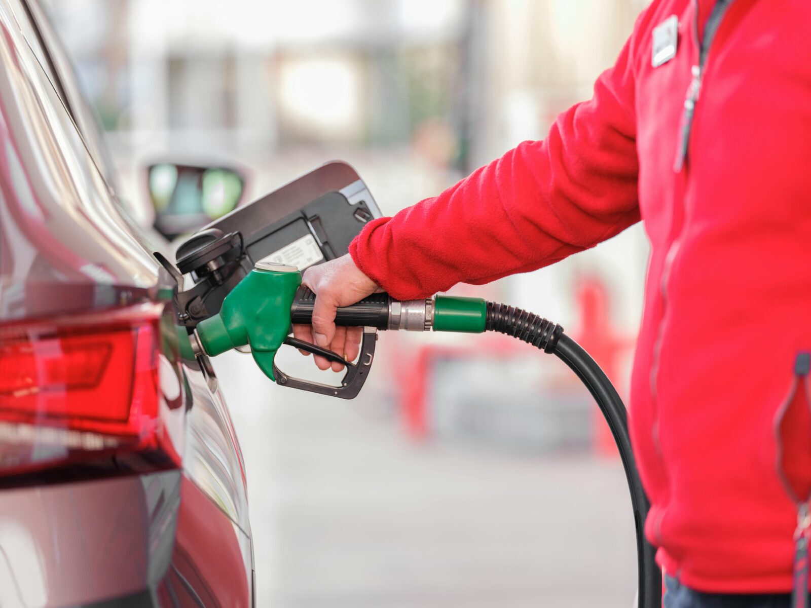 Close-up of a person refueling a car with a green hose at a gas station.